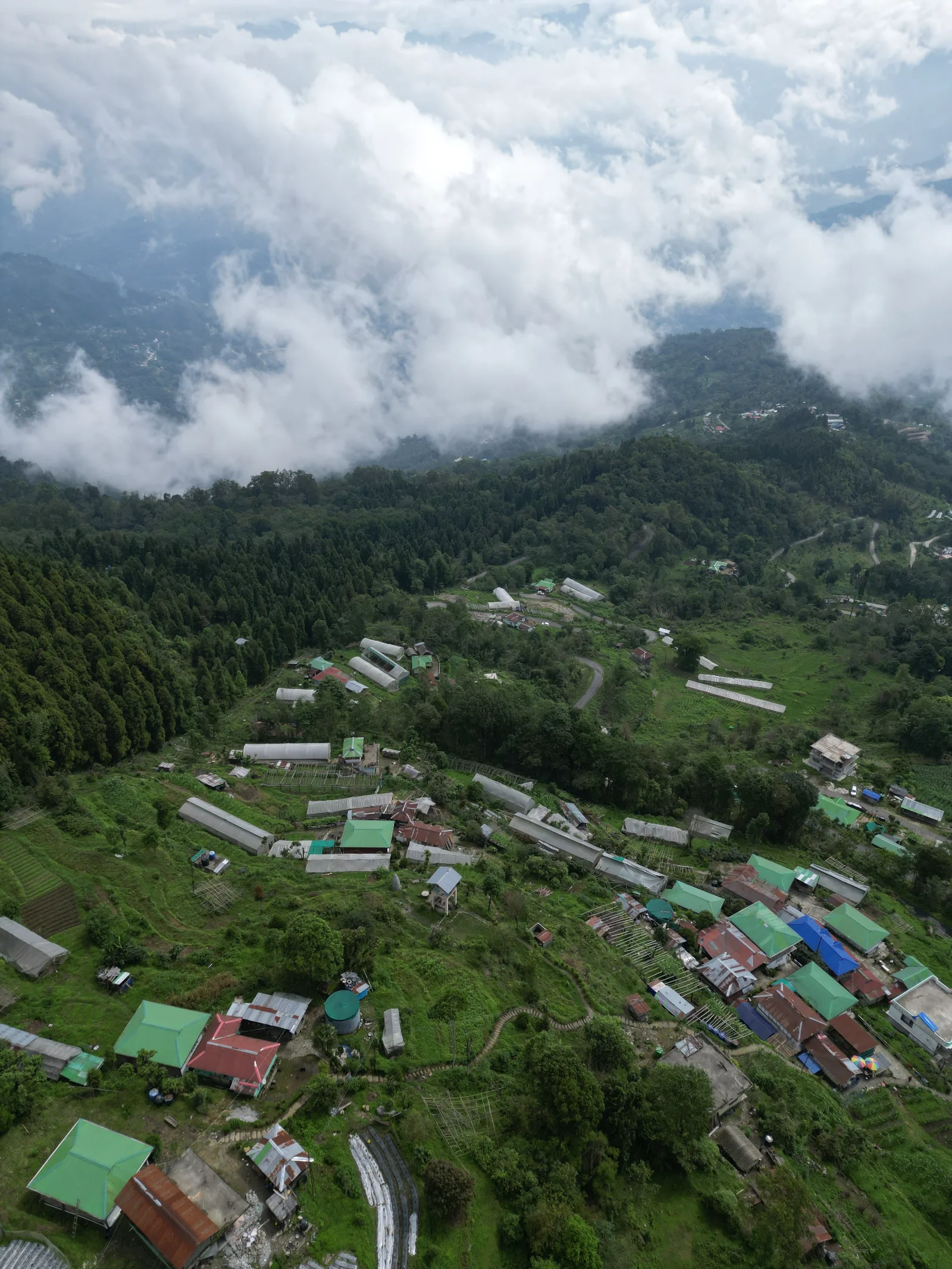 Aerial view of Yakten, its homes and polyhouses spread along the ridge under low cloud