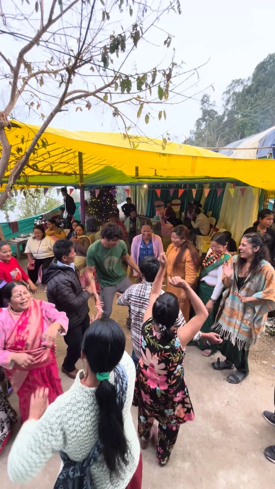 Villagers and guests dancing together under a yellow awning at a celebration