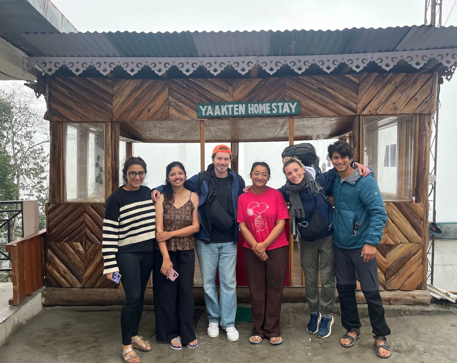 Guests standing with their host under the Yaakten Homestay sign on a misty morning