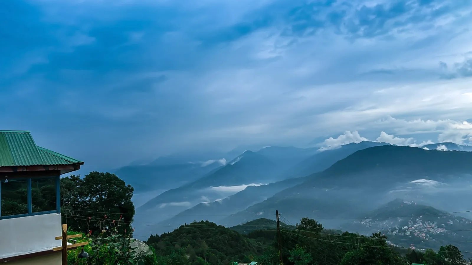 Cloud settling into the ridges below Yakten at dusk, a green-roofed homestay in the foreground