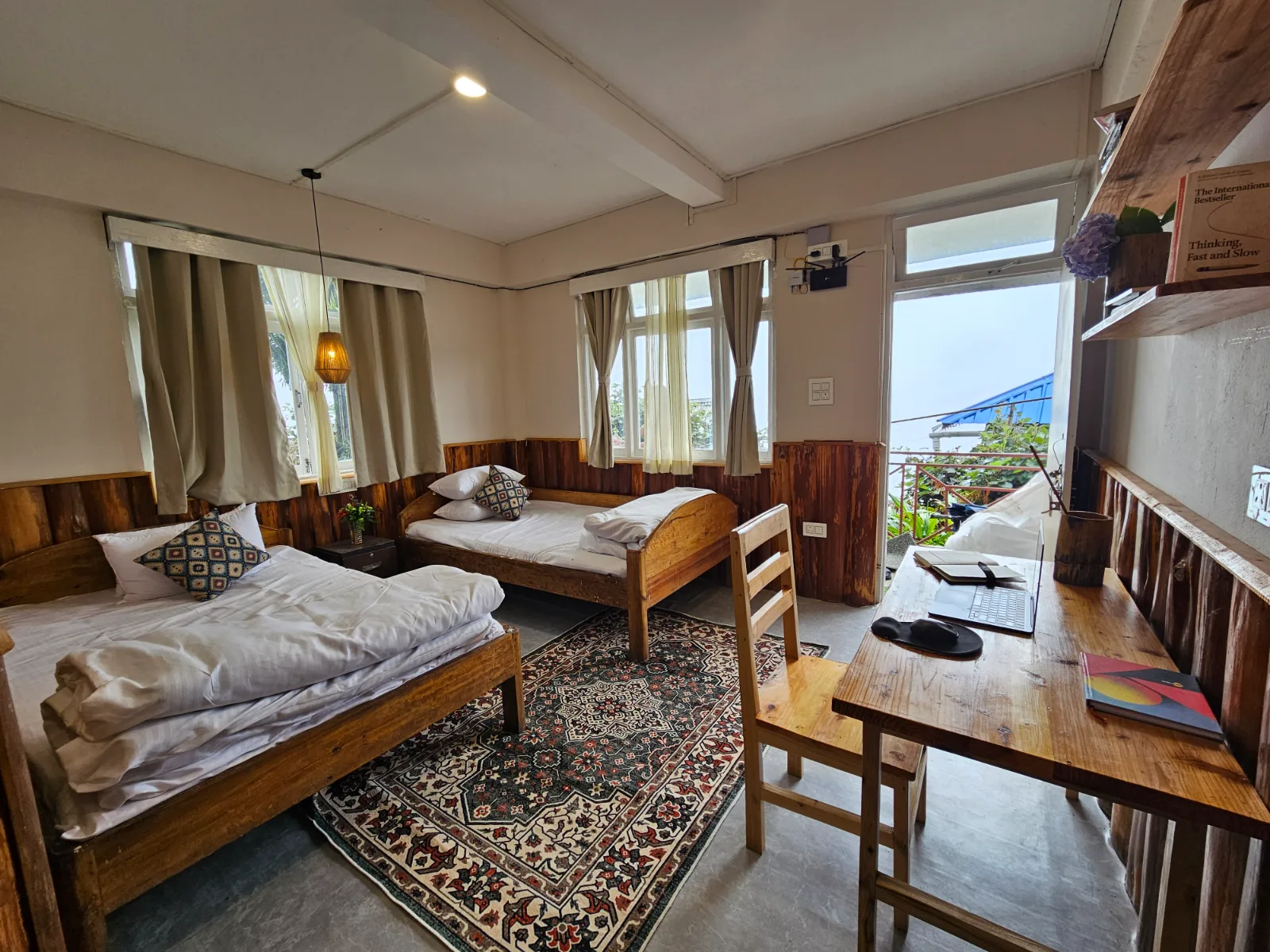 A room at Orchid homestay: pine panelling, two beds, and a desk set into the window looking out over the valley